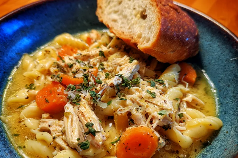 Chef Mitchell stirring a pot of Comforting Chicken Soup on the stove, with steam rising and ingredients visible.