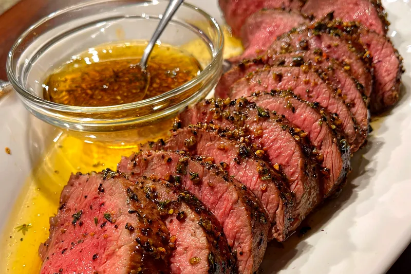Herb-crusted beef tenderloin being seared in a cast iron skillet before roasting, showing the golden-brown crust formation