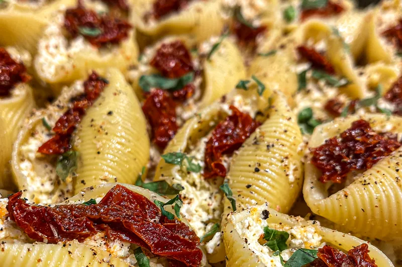 An array of ingredients including jumbo shells, ricotta cheese, sun-dried tomatoes, and fresh basil laid out for Sun-Dried Tomato Shells.